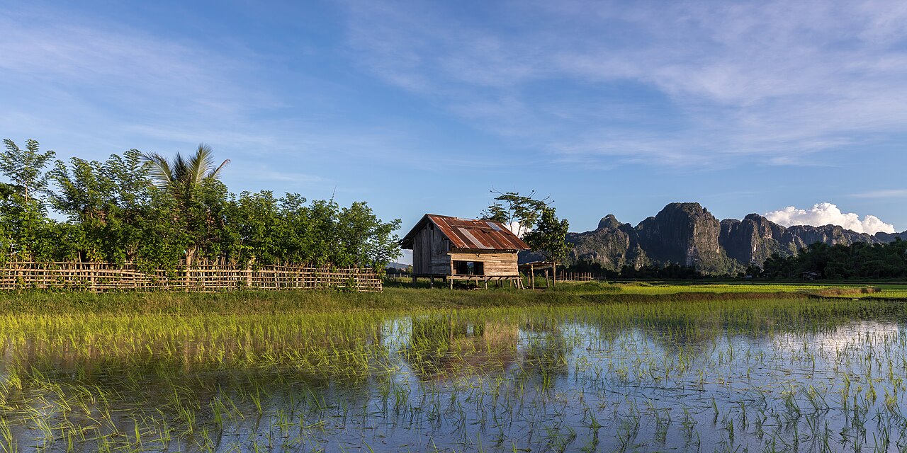 Wooden hut fence mountains and blue sky in the green rice fields of Vang Vieng in Laos, illustrative activity photo